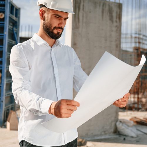 Working with document. Man in uniform is on the construction site.